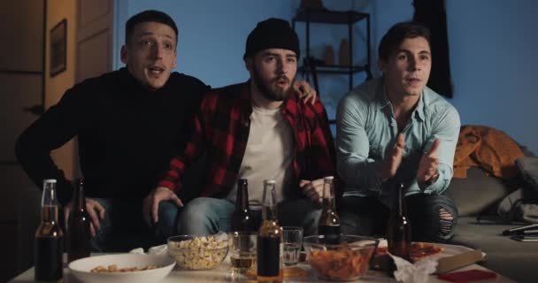 Tres amigos viendo el partido de fútbol en casa, animando al mejor equipo de fútbol. Emoción. Los fans de los hombres celebran ganar . — Vídeos de Stock