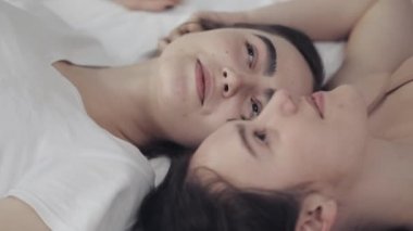 Mutlu lezbiyen kızlar yatakta yatıyorlar, gülümsüyorlar ve birbirlerinde eğleniyorlar. LGBT aile kavramı, yavaş hareket.