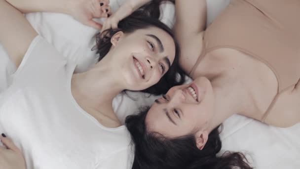 Happy lesbian girls are lying on the bed, smiling and enjoying each other. LGBT family concept, slow motion. Top view. — Stock Video