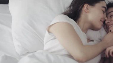 Lezbiyen çift evde yatakta birlikte yatarken sarılma ve gülümseyerek. Genç lezbiyenler uyandıktan sonra öper ve sarılır