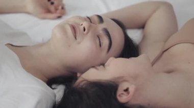 Mutlu lezbiyen kızlar yatakta yatıyorlar, gülümsüyorlar ve birbirlerinde eğleniyorlar. LGBT aile kavramı, yavaş hareket.