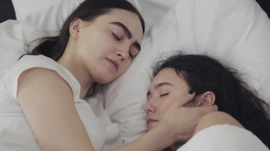 Lezbiyen çift evde yatakta birlikte yatarken sarılma ve gülümseyerek. Genç lezbiyenler uyandıktan sonra öper ve sarılır