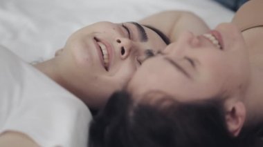 Mutlu lezbiyen kızlar yatakta yatıyorlar, gülümsüyorlar ve birbirlerinde eğleniyorlar. LGBT aile kavramı, yavaş hareket.