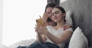 Mutlu lezbiyen çift video evde yatakta yatarken akıllı telefon sohbet. Nişan yüzüklerini romantik kutlamaların tadını çıkarırken gösteriyorlar. LGBT lezbiyen çift birlikte.