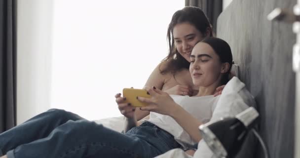 幸福的女同性恋夫妇躺在床上拥抱，在智能手机设备上看电影。Lgbt 女同性恋夫妇一起。慢动作. — 图库视频影像