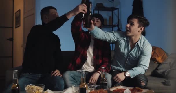 Három barát csinálás pirítós gesztus-val sör és néz foci párja-ra TV otthon. Érzelem, futballszurkolók — Stock videók
