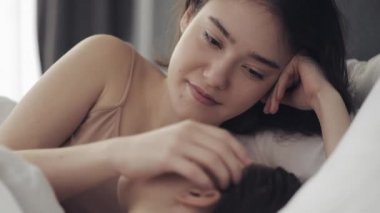 Lezbiyen çift evde yatakta birlikte yatarken sarılma ve gülümseyerek. Genç lezbiyenler uyandıktan sonra öper ve sarılır