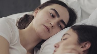 Lezbiyen çift evde yatakta birlikte yatarken sarılma ve gülümseyerek. Genç lezbiyenler uyandıktan sonra öper ve sarılır