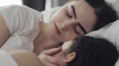 Lezbiyen çift evde yatakta birlikte yatarken sarılma ve gülümseyerek. Genç lezbiyenler uyandıktan sonra öper ve sarılır