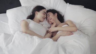 Lezbiyen çift evde yatakta birlikte yatarken sarılma ve gülümseyerek. Genç lezbiyenler uyandıktan sonra öpüşür ve sarılır. Üstte görüntü.