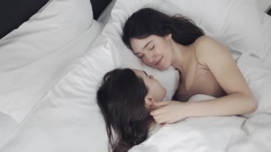 Lezbiyen çift evde yatakta birlikte yatarken sarılma ve gülümseyerek. Genç lezbiyenler uyandıktan sonra öper ve sarılır