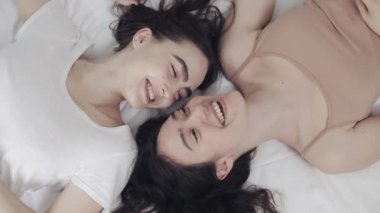 Mutlu lezbiyen kızlar yatakta yatıyorlar, gülümsüyorlar ve birbirlerinde eğleniyorlar. LGBT aile kavramı, yavaş çekim. Üstte görüntü.