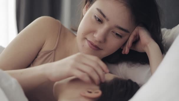 レズビアンのカップルは、自宅でベッドに一緒に横たわっている間、抱擁し、笑顔。若いレズビアンは目を覚ます後にキスと抱擁 — ストック動画