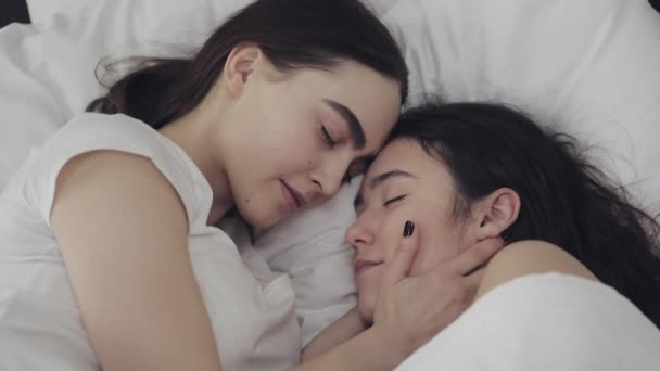 Lesbická dvojice se s úsměvem usmívala a ležela doma v posteli. Mladé lesbičky Polibky a hubičky po probuzení — Stock video