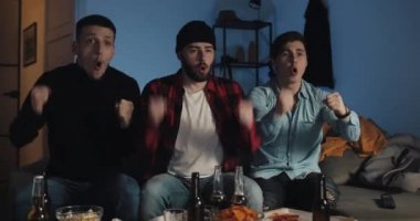 Evde televizyonda futbol maçı izleyen üç arkadaş, futbol taraftarları takımlarını destekliyor