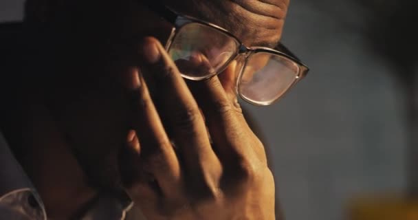 Cansado de trabajar en la computadora, el joven negro se levanta las gafas y se frota los ojos. Workaholic, trabajando duro. Noche. De cerca. . — Vídeos de Stock