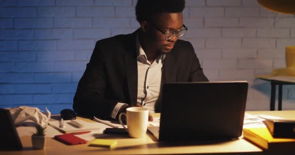 Jovem empresário negro com computador portátil e papéis a trabalhar no escritório nocturno. Ele assina os documentos. Negócio, workaholic, conceito do prazo . — Vídeo de Stock