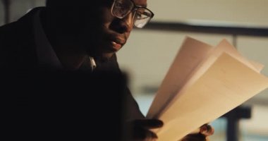 Yorgun genç siyah işadamı gece ofisinde belgelerle çalışıyor. Kağıtları analiz eden yakışıklı iş adamıportresi. İş, işkolik, son tarih kavramı