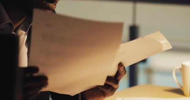 Joven hombre de negocios negro cansado trabajando con documentos en la oficina nocturna. Retrato del hombre de negocios guapo analizando papeles. Negocio, adicto al trabajo, concepto de plazo . — Vídeo de stock