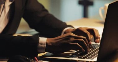 Yorgun genç siyah işadamı dizüstü bilgisayarda yazarak. Gece ofisinde çalışıyor. Steadicam atış.