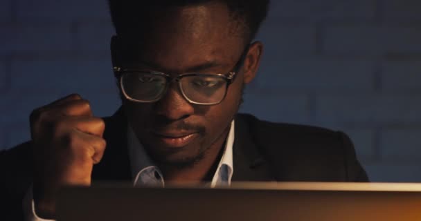 Cansado jovem empresário negro trabalhando com laptop no escritório da noite. Freelancer trabalhando até tarde no escritório do quarto escuro horas extras no laptop. Negócio, workaholic, conceito do prazo . — Vídeo de Stock