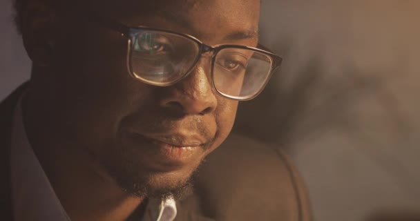 Hombre de negocios afroamericano concentrado en anteojos delante de la computadora portátil con reflejo de la exhibición en anteojos. Joven freelancer masculino trabajando de noche. De cerca. . — Vídeos de Stock