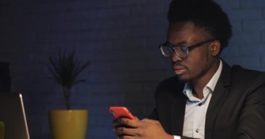 Genç işadamı gece ofisindeki masasında akıllı telefon kullanıyor..
