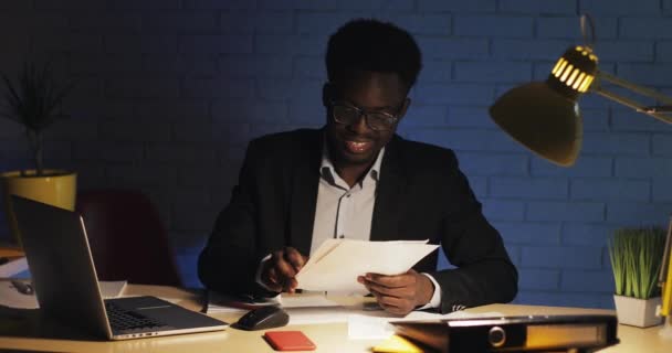 Νεαρός ευτυχισμένος επιχειρηματίας διαβάζει έγγραφα στο γραφείο του στο νυχτερινό γραφείο. Άνδρας που εργάζεται σε έγγραφα. — Αρχείο Βίντεο