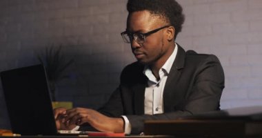 Kızgın Afro-Amerikalı işadamı gece geç saatlerde ofiste dizüstü bilgisayar üzerinde çalışıyor. Çalışmayı bitiriyor.