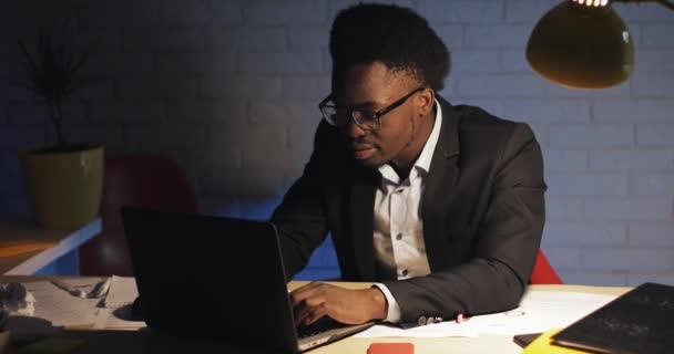 Молодой бизнесмен, работающий над ноутбуком в офисе поздно ночью. Он читает хорошие новости и заканчивает работу. . — стоковое видео