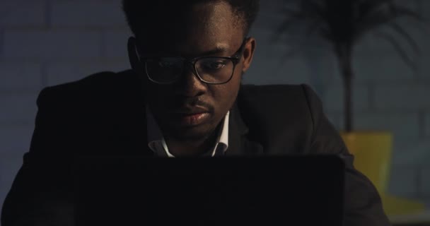 Fatigué de travailler sur l'ordinateur, le jeune homme noir lève ses lunettes et se frotte les yeux. Un accro du travail, qui travaille dur. Bonne nuit. Gros plan . — Video