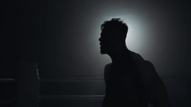 Boks eldivenli kızgın adam duygusal olarak boks ringinde duruyor. Yavaş, hareket, siluet. Boks konsepti.
