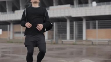 Kameraya koşan genç çekici adam. Sonra durur, Bükümler. Ağır nefes alıyor. Akıllı saatin sonucunu izliyor. Bulanık arka plan, yakın çekim.
