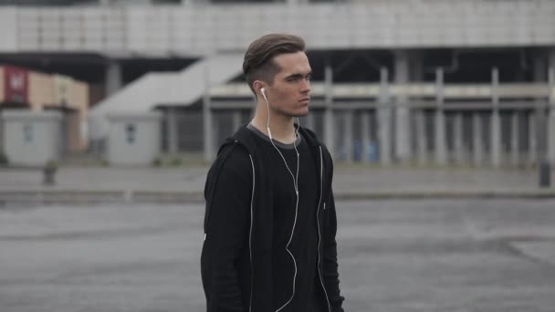 Portrait de coureur masculin attrayant avec des écouteurs fonctionnant à l'arrière-plan du stade. Athlète tourne la tête et regarde dans la caméra. Fitness sain homme athlétique jogging en plein air . — Video