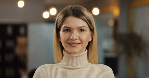 Ofis çalışma alanında duran kameraya bakan genç başarılı iş kadını portresi.