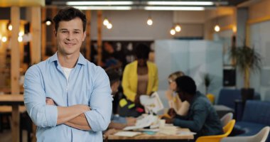 Portrait of young smiling successful businessman standing in modern office. Working people on the blurred background.