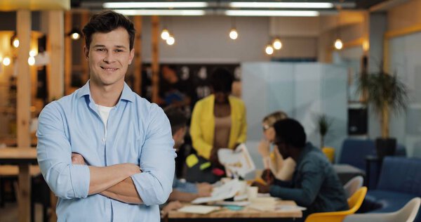 Portrait of young smiling successful businessman standing in modern office. Working people on the blurred background. — Stock Photo, Image