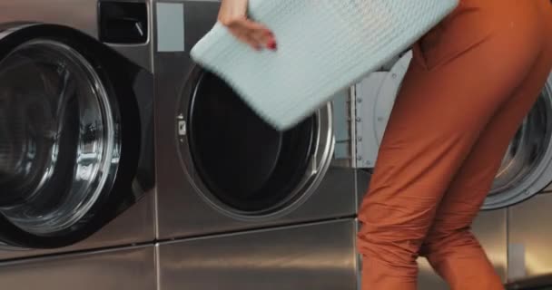 De gelukkige jonge Afrikaanse Amerikaanse vrouw zit voor een wasmachine en laadt de wasmachine met vuile Wasserij. Zelfbedienings openbare Wasserij. — Stockvideo