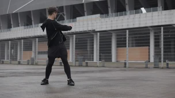 Attractive male athlete does morning exercise outdoors close up slow motion in the cloudy weather. Workout standing on the street near sports stadium. Healthy lifestyle will power motivation concept. — Stock Video