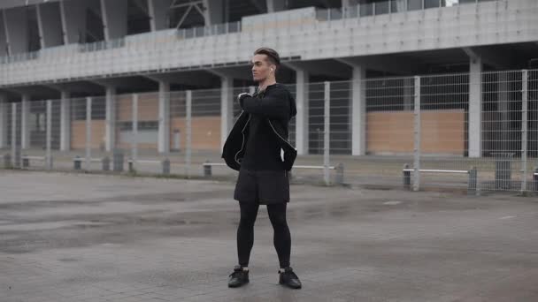 Atractivo atleta masculino hace ejercicio de la mañana al aire libre cerca de cámara lenta en el clima nublado. Entrenamiento de pie en la calle cerca del estadio deportivo. Estilo de vida saludable voluntad poder motivación concepto . — Vídeo de stock