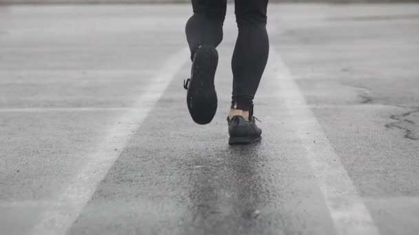 Slow motion shot of legs of a runner in sneakers. Male sports man jogging outdoors. Single runner running in rainy weather. Close up. — Stock Video