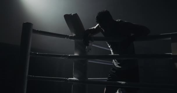 Trött manlig boxare med flaska vatten vilar på ämnet i ringen. Silhuett. Boxning Concept. — Stockvideo