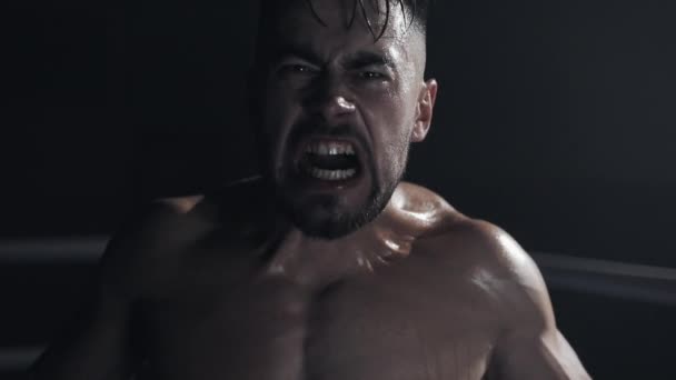 Angry man with boxing gloves screams emotionally looking ar the camera standing on the boxing ring. Slow motion. — Stock Video