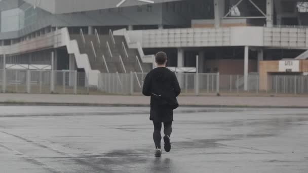 Attraktiver junger Mann, der mit Kopfhörern in Zeitlupe nach draußen läuft. Regenwetter. Ausdauertraining. Gesunder Lebensstil - Laufen. — Stockvideo