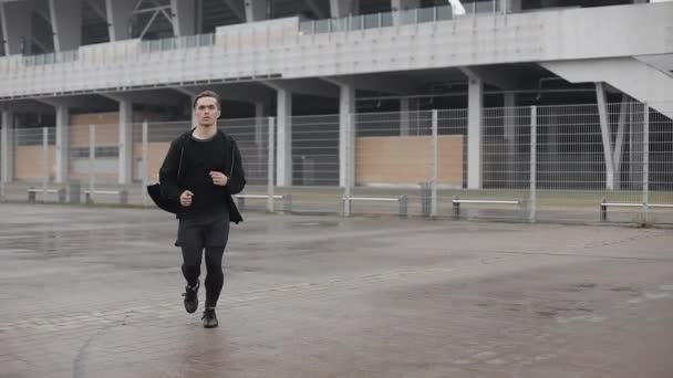 Attraktiv ung man kör utomhus slow motion. Han tittar in i kameran. Regnigt väder. Konditionsträning träning. Hälsosam livsstil-löpning. — Stockvideo