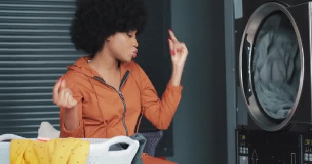 Jonge gelukkige Afro-Amerikaanse vrouw met krullend haar grappig dansen in de self-service openbare Wasserij. — Stockvideo