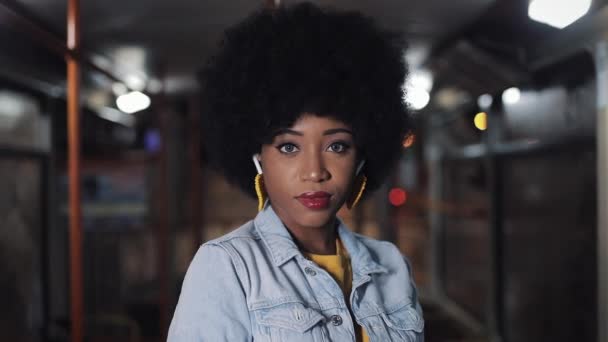Afrikanerin blickt in die Kamera, die in den öffentlichen Verkehrsmitteln steht, Steadicam-Aufnahme. Nahaufnahme. Hintergrund Stadtbeleuchtung. — Stockvideo