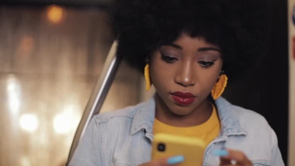 有吸引力的年轻非洲裔美国妇女拿着扶手,在公共交通工具上使用智能手机。夜晚时间。特写。城市灯光背景. — 图库视频影像