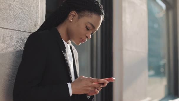 Eine elegante Afro-Geschäftsfrau steht mit ihrem Smartphone auf der Straße in der Nähe des Geschäftszentrums. schwarz stilvoll. Dreadlocks. Afro-Frisur. — Stockvideo