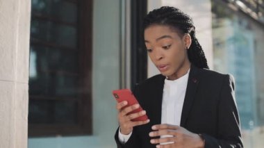 Şık afro iş kadını iş merkezi yakınında sokakta duran akıllı telefon kullanarak. Siyah Şık. Dreadlocks. Takım elbiseli kadın profesyonel akıllı telefondan haber sahibi.